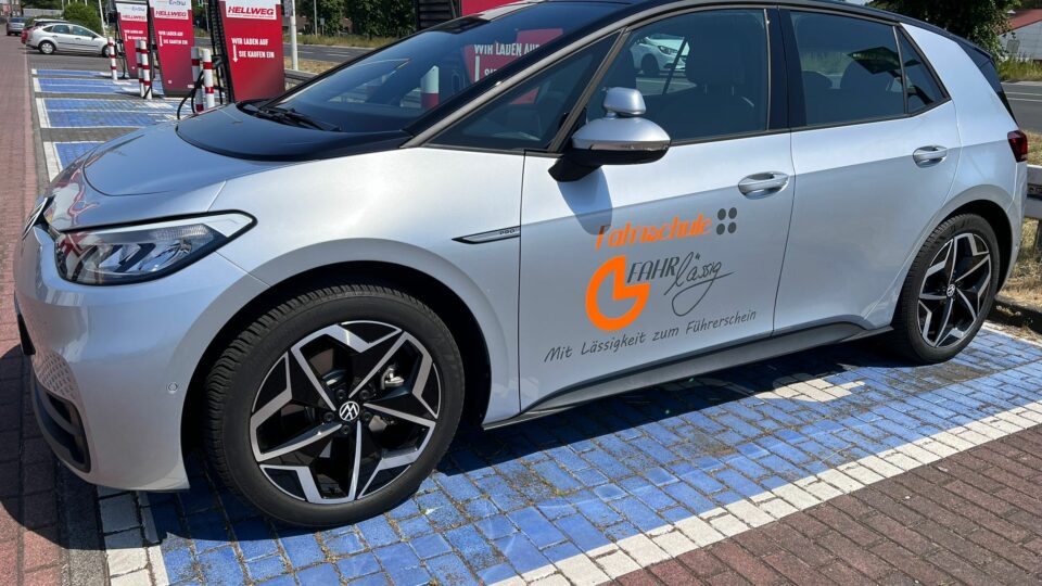 Elektrisches Fahrschulauto der Fahrschule FAHRlässig beim Laden an einer EnBW-Ladestation, mit Logo und Slogan Mit Lässigkeit zum Führerschein