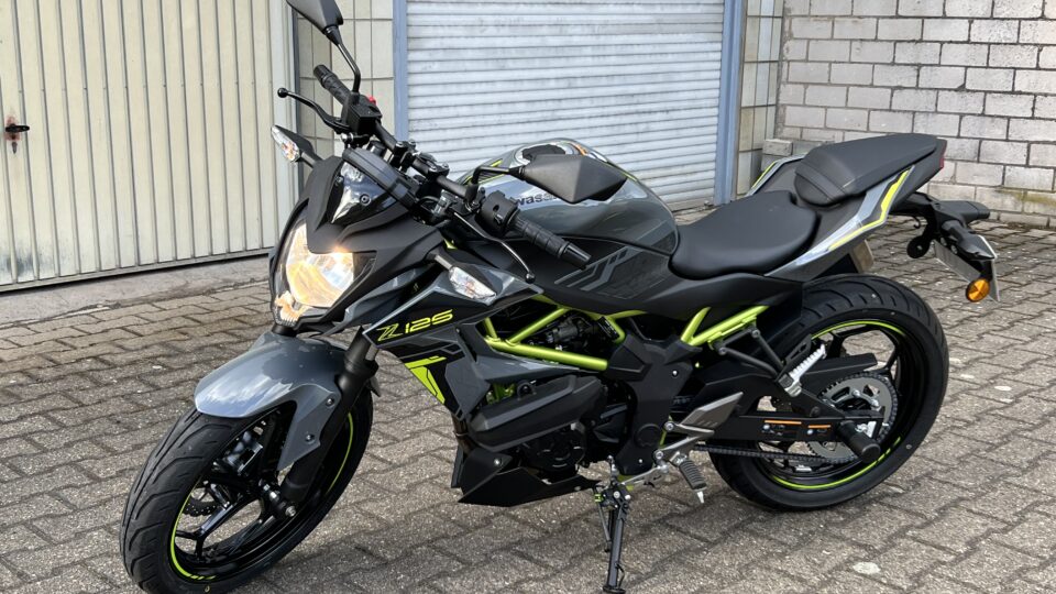 Kawasaki Z125 Motorrad mit grün-schwarzem Design, auf einem gepflasterten Hof vor einer Garage abgestellt.