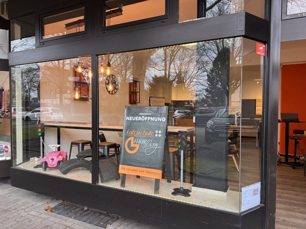Außenansicht der Fahrschule mit großer Fensterfront und Schild zur Neueröffnung, einladend und modern gestaltet.