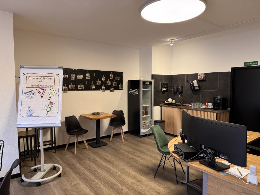 Schulungsbereich der Fahrschule mit Flipchart zu Verkehrsregeln und gemütlicher Küchenzeile.
