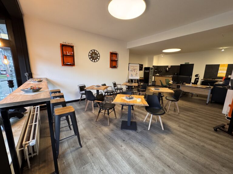 Moderner Unterrichtsraum der Fahrschule mit Holztischen, hoher Theke und dekorativen Elementen wie Verkehrszeichen und Uhr