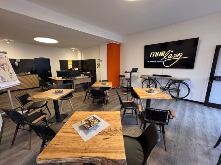 Moderner Schulungsraum der Fahrschule mit Holztischen und großem Bildschirm mit FAHRlässig-Logo.